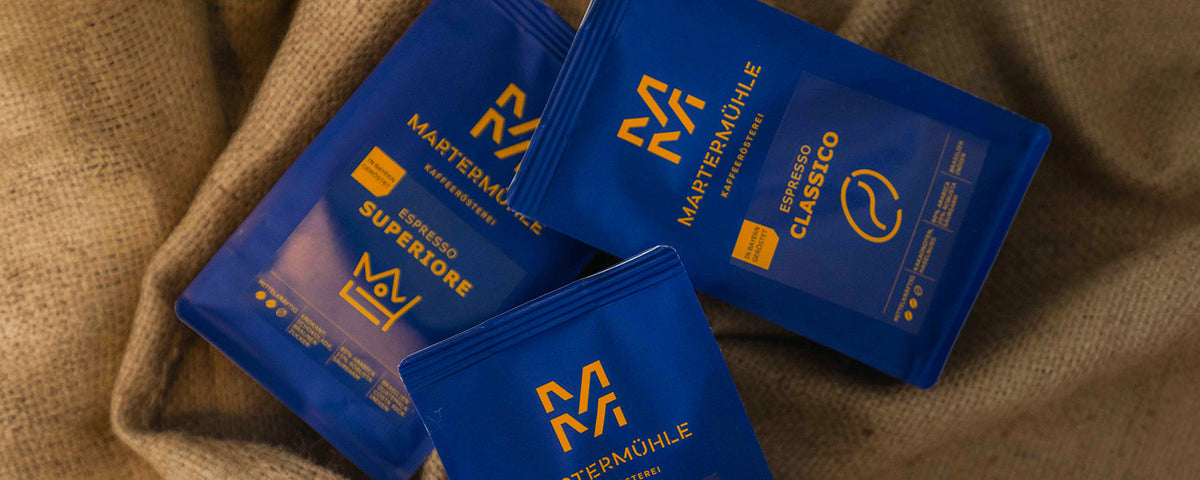 Drei blaue Espressotüten der Kaffeerösterei Martermühle liegen auf Kaffeesäcken