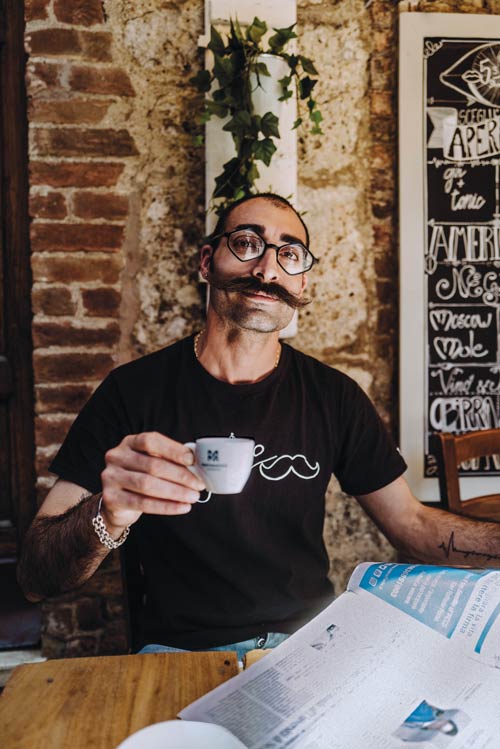 Mann mit auffälligem Schnurrbart und eckiger Brille der Zeitung liest und dabei einen Martermühle Espresso trinkt.