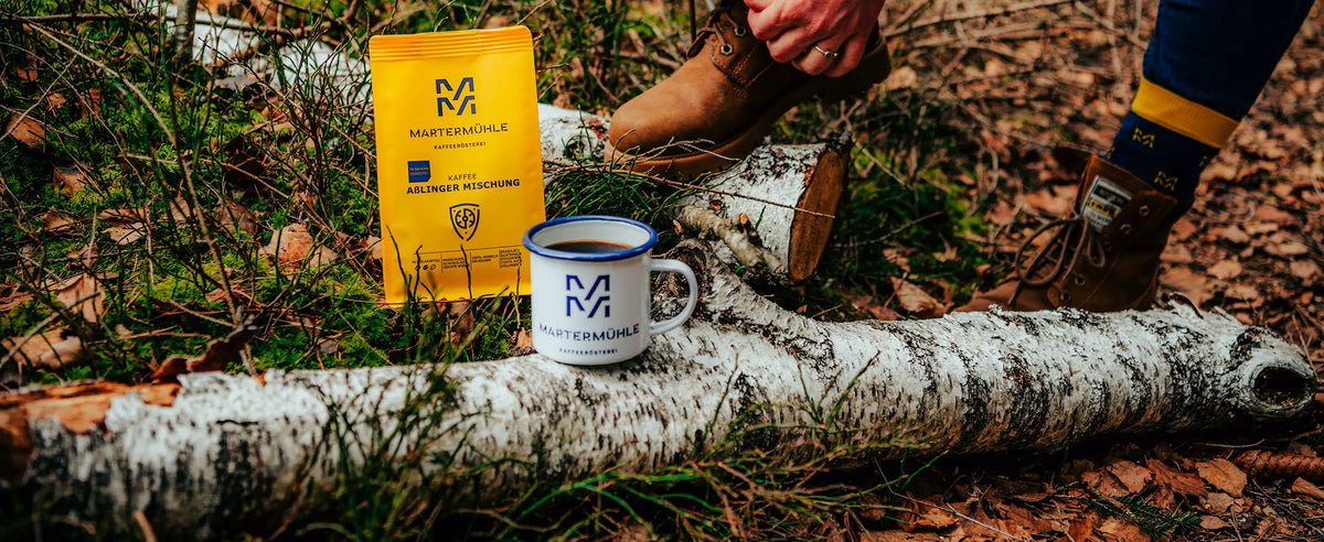 Kaffee Aßlinger Mischung in der Natur mit einer Martermühle Tasse.