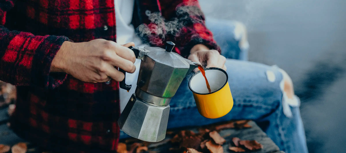 Junger Mann schenkt sich Kaffee aus einem Espressokocher in eine gelbe Martermühle Tasse ein.