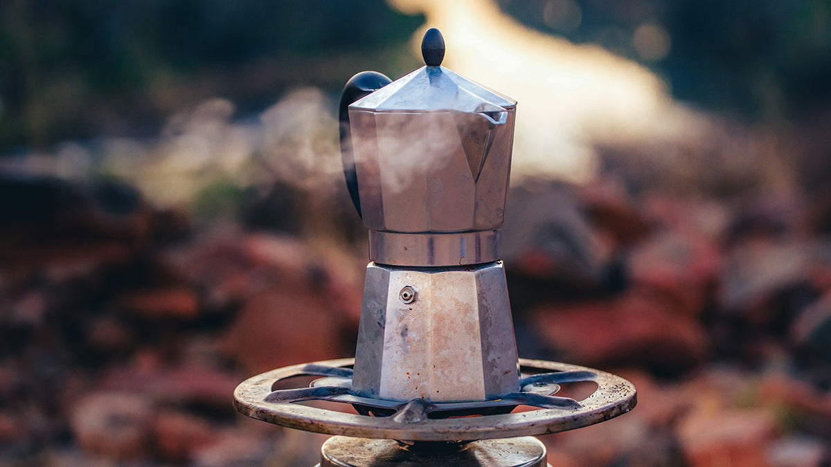 Espressokocher in der Natur, der auf einem Gaskocher steht und dampft.